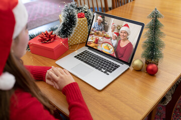 Poster - Caucasian woman in santa hat making christmas laptop video call with smiling family at dinner table