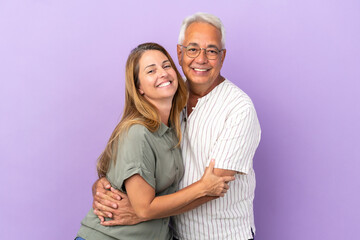 Wall Mural - Middle age couple isolated on purple background hugging