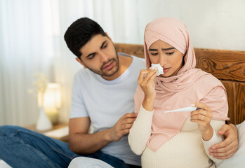 Illness during pregnancy. Loving muslim husband taking care about his sick pregnant wife, woman measuring temperature