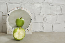 Bitten Green Apple Near Mirror With Reflection Of Whole Fruit On Table, Space For Text