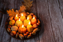 Burning Pumpkin Shape Candles, Acorns, Nuts On Plate, Dark Wooden Background. Autumn Seasonal Composition. Symbol Of Harvest, Mabon, Thanksgiving Holiday, Halloween. Fall Time. Witch Magic Ritual