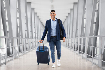 Air Travels. Portrait Of Smiling Arab Man Walking With Luggage At Airport