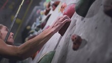 Sport Athletic Woman Climbs Up An Artificial Rock Wall. Climbing Solo In Indoor Gym. The Girl Grabs A Stone With Her Hand. Hobby In The City, Healthy Lifestyle. Slow Motion