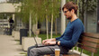 © RecCameraStock - Young business man using laptop while sitting outdoor city park. Student studying on a bench. Entrepreneur working on laptop.