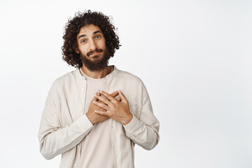 Wall Mural - Cute and caring adult man, holding hands on heart, looking touched and flattered, grateful for something, standing over white background