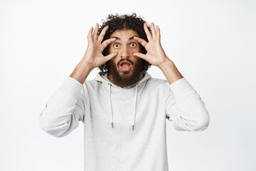 Wall Mural - Shocked hispanic man widen his eyes in awe, cant believe, looking with disbelief and amazement at camera, standing startled over white background