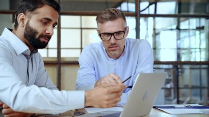 Two diverse business men discussing financial market data using laptop and digital tablet. Financial advisor broker manager consulting investor client about digital investment at office meeting.