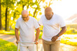 © Acronym - Caregiver is teaching old man to walk with walker. Professional nurse and patient walking outdoor at sunset. Assistance, rehabilitation and health care.