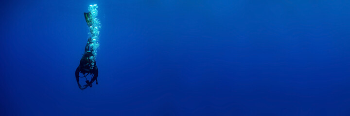 Blue background banner with a scuba diver entering water in a vertical position making bubbles 