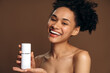 © speed300 - Brunette multiracial lady using cosmetic product. Happy girl holding bottle with body lotion and showing it to the camera with pleasure smile