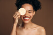 © speed300 - Portrait of multiracial woman hiding her eye behind the sponge while posing against brown background. Cosmetology, beauty and spa concept