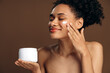 © speed300 - Attractive young woman closed her eyes and holding bottle with moisturizer while applying cream at her face. Girl with perfect face skin posing with smile
