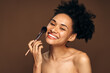 © speed300 - Close up of brunette lady holding make up brush near her face and smiling toothy to the camera. Beauty procedures concept. Stock photo