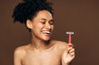 © speed300 - Horizontal view of carefree young woman laughing and looking at the razor. Portrait of smiling woman with naked shoulders smiling toothy. Beautiful girl isolated on beige background