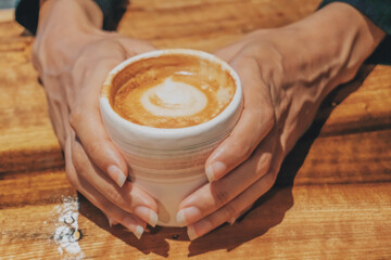 Wall Mural - Woman holding a coffee cup on a wooden table