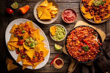 Wall Mural - Mexican food concept: tortilla chips, guacamole, salsa, chilli con carne and fresh ingredients over wooden background, top view
