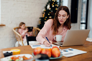 Young woman works at home while her daughter stays home on winter vacation