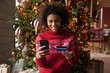 © fizkes - Happy African American woman do shopping use smartphone and credit card on New Year winter season sales. Smiling biracial female order online on cellphone, buy on Christmas discounts on web.