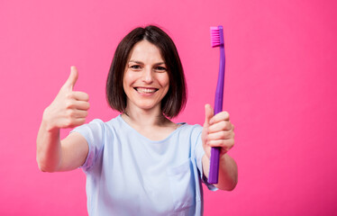 Wall Mural - Beautiful happy young woman with big toothbrush on blank pink background