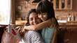 © fizkes - Happy Latin mom and daughter girl celebrating mothers day, 8 march, birthday, hugging on couch at home, receiving gift. Kid giving handmade greeting card to grateful mommy. Motherhood concept