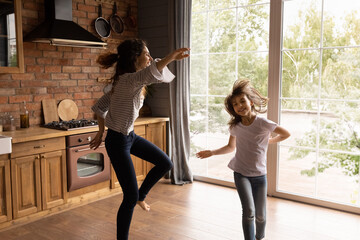 Wall Mural - Excited crazy young mom and daughter girl dancing to music in kitchen, having fun at home together, enjoying indoor activities, exercises, funny fitness, listening radio, singing song, going wild