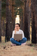 © Larisa - A girl is sitting with a laptop on her lap and biting a ripe red apple in a pine forest. The concept of remote work and training
