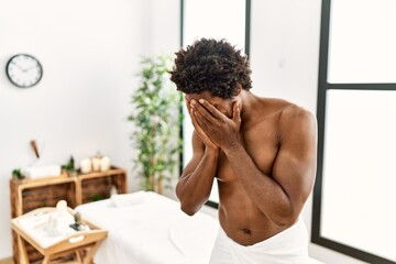 Poster - Young african american man shirtless wearing towel standing at beauty center with sad expression covering face with hands while crying. depression concept.