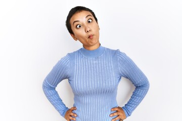 Wall Mural - Young hispanic woman with short hair standing over isolated background making fish face with lips, crazy and comical gesture. funny expression.