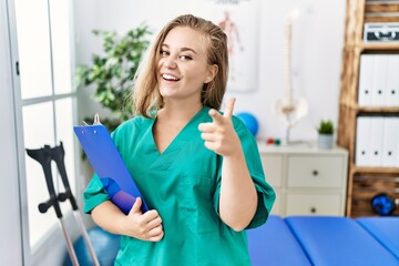 Wall Mural - Young caucasian woman working at pain recovery clinic pointing fingers to camera with happy and funny face. good energy and vibes.