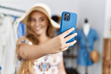 Young blonde girl wearing hat make selfie by the smartphone at clothing store