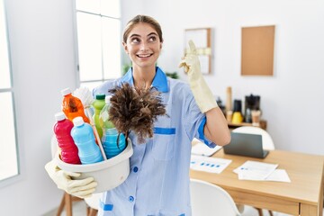 Sticker - Young blonde woman wearing cleaner uniform holding cleaning products pointing finger up with successful idea. exited and happy. number one.