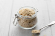 Nutritional yeast flakes in a glass jar on a white wooden background , selective focus