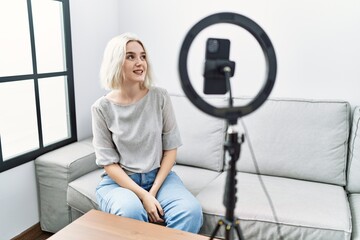 Sticker - Young caucasian woman recording vlog tutorial with smartphone at home looking away to side with smile on face, natural expression. laughing confident.