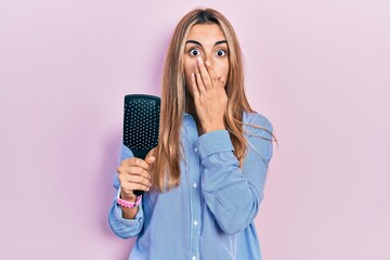 Canvas Print - Beautiful hispanic woman holding hairbrush covering mouth with hand, shocked and afraid for mistake. surprised expression