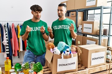 Sticker - Young gay couple wearing volunteer t shirt at donations stand doing money gesture with hands, asking for salary payment, millionaire business