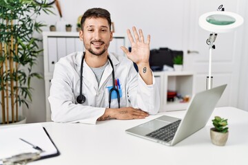 Sticker - Young doctor working at the clinic using computer laptop showing and pointing up with fingers number five while smiling confident and happy.