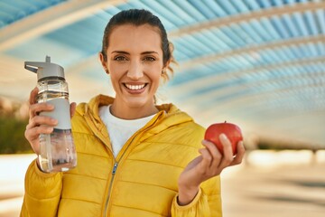 Young hispanic girl drinking bottle of water and eating apple at the city.