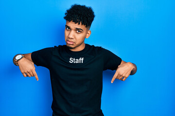 Young african american man wearing staff t shirt pointing down looking sad and upset, indicating direction with fingers, unhappy and depressed.