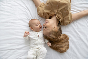 top view loving young mother and baby lying on bed white sheet, happy caring mom with little first c