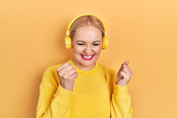 Canvas Print - Young blonde woman listening to music using headphones excited for success with arms raised and eyes closed celebrating victory smiling. winner concept.