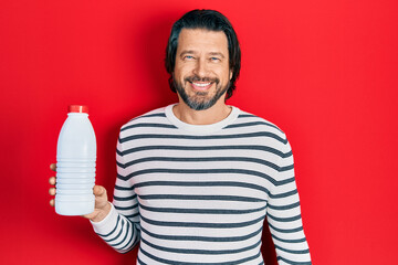 Canvas Print - Middle age caucasian man holding liter bottle of milk looking positive and happy standing and smiling with a confident smile showing teeth