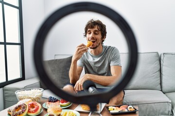 Sticker - Young hispanic man smiling confident eating fast food at home