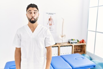 Sticker - Young handsome man with beard working at pain recovery clinic making fish face with lips, crazy and comical gesture. funny expression.