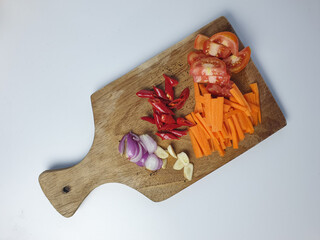 sliced onion, garlic, red pepper, carrot and tomato on wooden cutting board isolated on white background. cooking and seasoning concept