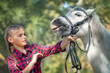 a teenage girl is afraid of a horse while training and caring for a pony. She holds the animal by the reins with an emotion of surprise and excitement and fear