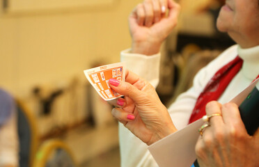 Old lady playing Bingo. Elderly woman's hands holding cardboard from bingo game at an event. Bingo player. Living room game. Classic board game. Entertainment. Woman's hands.