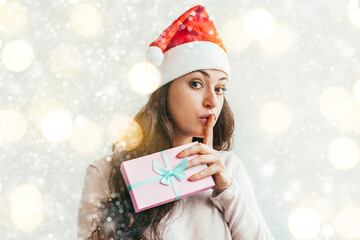 Wall Mural - Beautiful girl in red Santa Claus hat holding pink gift box makes gesture silence shh secret isolated on white background. Winter portrait of young woman. Happy Merry Christmas, secret Santa concept.