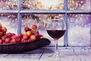 Bunch of purple grapes , glass of red wine or juice stand on wooden table against window. Red grape on a plate. Harvest in vineyard. Romantic evening at home. Still Life with fruit Alcoholic Beverage.