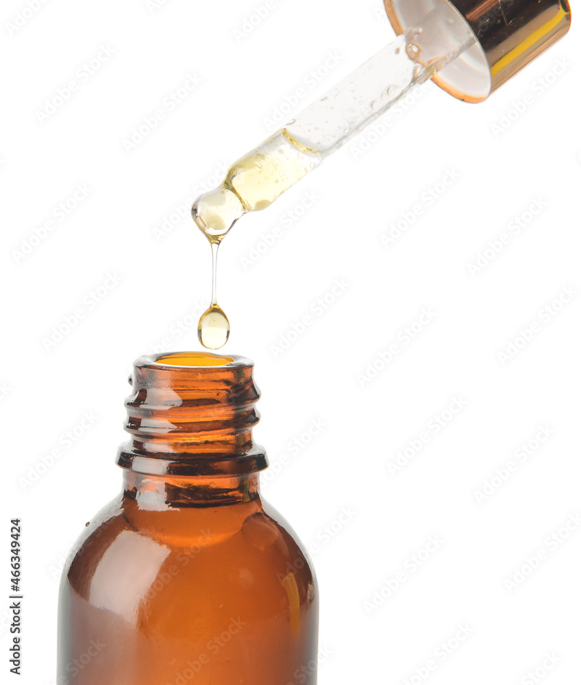 Dripping of essential oil from pipette into bottle on white background