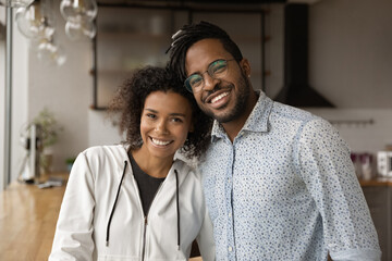 Wall Mural - Portrait of sincere smiling millennial generation loving african american family couple embracing posing in own modern home. Happy young affectionate biracial homeowners celebrating new beginning.